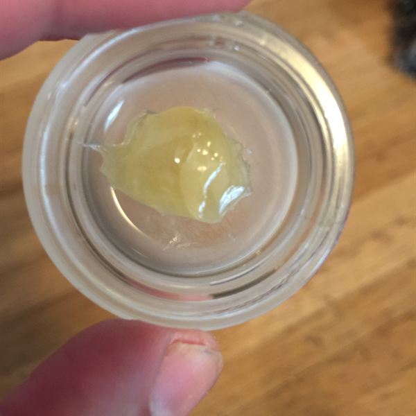 Pale gold rosin chip in a clear jar held over a wood table